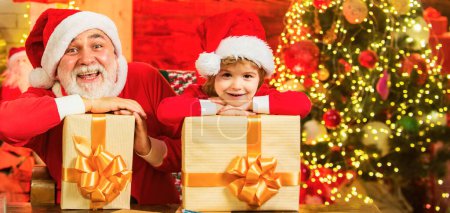 Photo for Funny little Santa grandfather and son holding bag with presents. Santa child grandfather and grandson. Child play with real grandfather Santa near christmas tree - Royalty Free Image