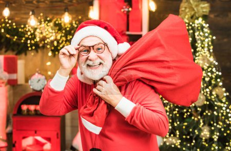 Foto de Hombre barbudo divirtiéndose cerca del árbol de Navidad en el interior. Retrato de invierno de Santa. Preparación de Navidad - Papá Noel celebrando el Año Nuevo - Imagen libre de derechos