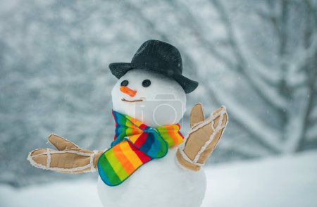 Téléchargez les photos : Joyeux bonhomme de neige souriant par une journée ensoleillée d'hiver. Bonhomme de neige fait main dans la neige en plein air. Bonhomme de neige en écharpe et chapeau. Bonhommes de neige mignons debout en hiver paysage de Noël. - en image libre de droit