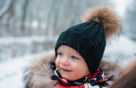 Téléchargez les photos : Funny laughing baby in winter outside. Cute toddler kid in a warm snowsuit and hat discovered winter forest. Snow, red cheeks, smile on face - en image libre de droit