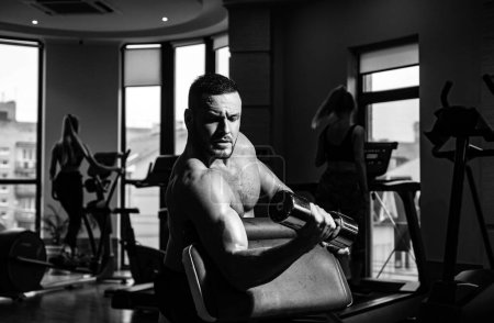 Photo for Portrait of young athlete doing exercise with dumbbell at the gym. Man training with dumbbells. Muscular guy exercises with dumbbells. Muscles with dumbbell - Royalty Free Image