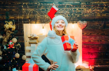 Photo for Christmas tree decorate at home. Smiling woman decorating Christmas tree at home. Open Mouth. Christmas happy. Happy woman. Christmas decorations and gift box on wooden background - Royalty Free Image