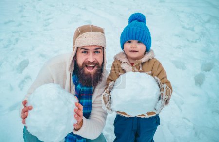 Foto de Papá e hijo jugando juntos al aire libre. Padre e hijo de invierno. Niño feliz jugando con bola de nieve sobre fondo blanco de invierno. Escena de invierno sobre fondo de nieve blanca - Imagen libre de derechos
