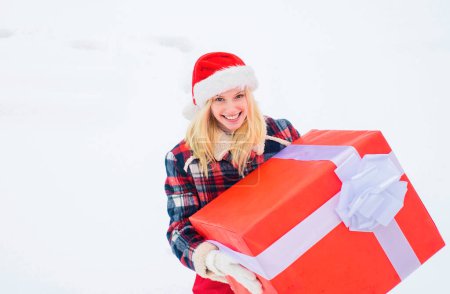 Foto de Chica de Navidad sosteniendo un gran regalo. Loca chica de Navidad empuja un gran regalo en el fondo de invierno de nieve. Feliz Navidad y Felices Fiestas - Imagen libre de derechos