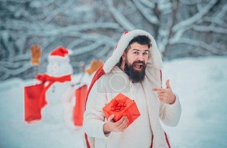 Téléchargez les photos : Père heureux jouant avec un bonhomme de neige lors d'une promenade hivernale enneigée. Drôle de gens d'hiver Portrait. Mode homme avec boîte cadeau de Noël - en image libre de droit