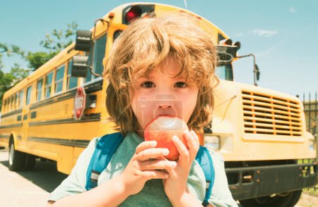 Foto de De vuelta a la escuela. Niño de la escuela en la parte delantera del autobús escolar comer manzana - Imagen libre de derechos