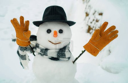 Foto de Muñeco de nieve feliz con cajas de regalo de pie en invierno paisaje de Navidad. Banner de venta de vacaciones de invierno. Lindo muñeco de nieve en sombrero y bufanda en el campo cubierto de nieve - Imagen libre de derechos