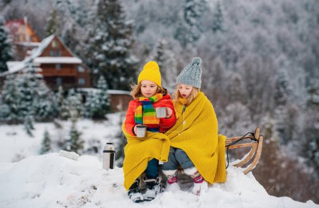 Téléchargez les photos : Enfant garçon et petite fille profitant d'une balade en traîneau. Les enfants font de la luge ensemble, jouent dehors dans la neige sur les montagnes en hiver. Enfants frère et sœur en vacances de Noël - en image libre de droit