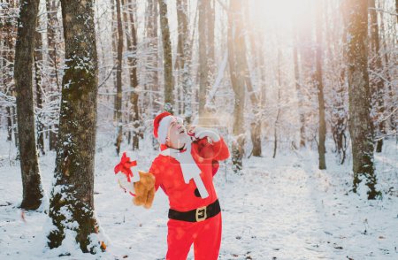 Photo for Real Santa Claus in red cap pulling large red gift sack. Santa magical fog walking along the field - Royalty Free Image