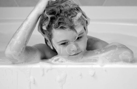 Foto de Champú para niños. Niño en el baño con burbujas. Niño feliz disfrutando del baño. Niño sonriendo en el baño con espuma de jabón. El niño se baña en un baño con espuma - Imagen libre de derechos
