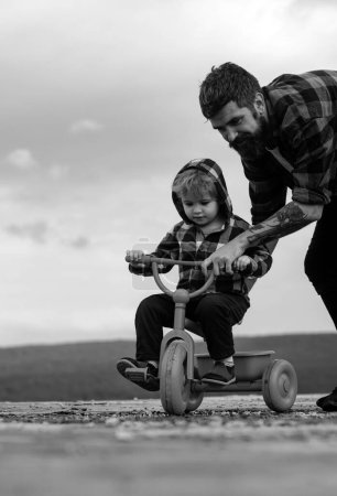 Téléchargez les photos : Père apprenant à son fils à faire du vélo. Le petit garçon apprend à faire du vélo avec son père. Papa enseignant fils à faire du vélo - en image libre de droit