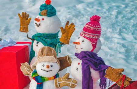 Téléchargez les photos : Jolie famille de bonhommes de neige avec - cadeaux debout dans le paysage de Noël d'hiver. Carte de voeux d'art festif. Famille des bonhommes de neige - cadeau présente concept. Bannière Nouvel An. Émotions cadeaux - en image libre de droit