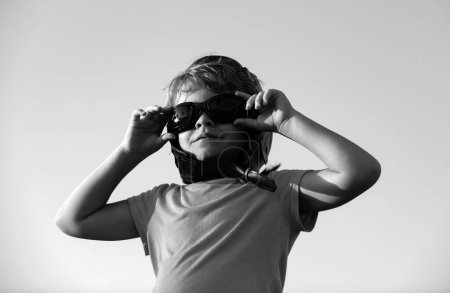 Téléchargez les photos : Petit garçon avec lunettes de pilote et casque, garçon veut devenir pilote et astronaute. Joyeux jeu d'enfant sur le ciel. Enfants pilote rêve de voler - en image libre de droit