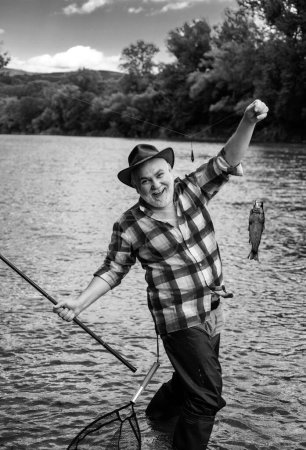 Téléchargez les photos : Happy old fisherman caught a trout fish. Portrait of cheerful smiling senior man fishing. Grandfather with catch fish - en image libre de droit