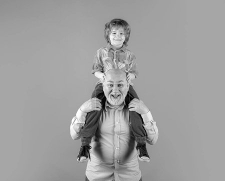 Photo for Young grandson and old grandfather piggyback with funny face isolated on blue in studio. Granddad and cute boy with funny face - Royalty Free Image