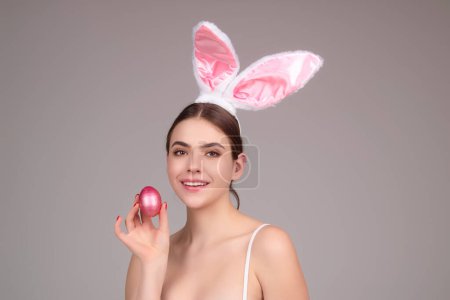 Téléchargez les photos : Woman with bunny ears and easter eggs. Easter bunny isolated on studio background. Holidays, spring and party concept. Portrait of cute girl celebrating Easter - en image libre de droit