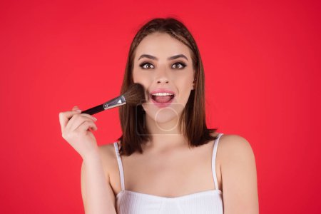 Téléchargez les photos : Girl hold blush blusher apply powder visage isolated over studio background. Young woman powdering cheeks. Makeup brush. Female model gets blush powder on the cheekbones - en image libre de droit