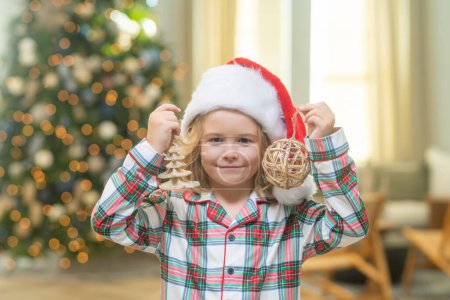 Téléchargez les photos : Joyeux Noël les enfants. Noël et vacances d'hiver à la maison. Petit garçon mignon décoré sapin de Noël. Enfants avec boule et jouets près de l'arbre de Noël dans la chambre - en image libre de droit
