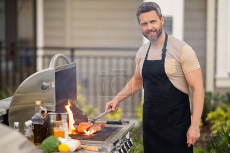 Photo for Hispanic man cooking on barbecue in the backyard. Chef preparing barbecue. Barbecue chef master. Handsome man preparing barbecue, bbq meat. Grill and barbeque - Royalty Free Image
