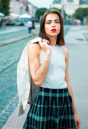 Téléchargez les photos : Belle modèle féminin tenir le costume blanc à travers sholder dans la ville d'été en Europe. Femme branchée posant sur le fond de la rue - en image libre de droit