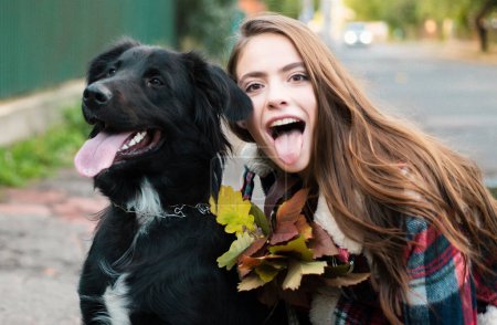 Foto de Chica feliz consigue perro encantador, juega y abraza. Humanos y perros. Chica con lengua abrazando cachorro perro al aire libre - Imagen libre de derechos