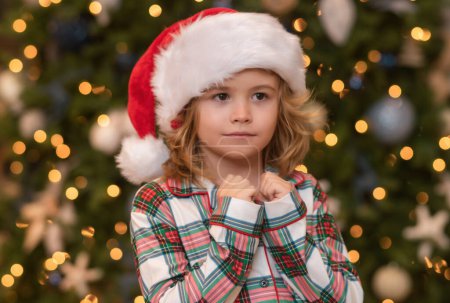 Foto de Niño rezando, niños orando.Feliz niño divertido en el sombrero de Santa cerca del árbol de Navidad. Concepto de Navidad y Año Nuevo - Imagen libre de derechos