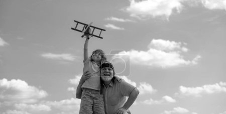 Téléchargez les photos : Grand-père et fils avec avion jouet sur fond bleu ciel et nuages. Hommes génération grand-père et petit-fils jouer à l'extérieur - en image libre de droit