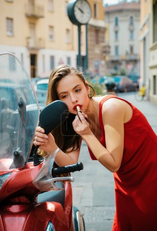 Photo for Fashion street. Makeup in motion. Girl put lipstick looking in mirror of motorcycle - Royalty Free Image