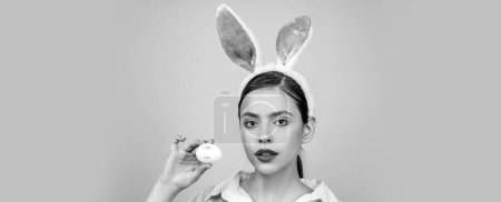 Foto de Banner de Pascua con mujer conejita. Lápiz labial beso huella en huevo de Pascua. Conejita de Pascua mujer, conejo y niña. Retrato de una mujer feliz con orejas de conejo. Caza de huevos - Imagen libre de derechos
