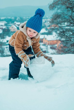 Foto de Niño feliz jugando con nieve en una caminata invernal nevada. Lindo niño en el helado parque de invierno. Niño de invierno. Niño jugando con nieve en el parque. Retrato de invierno de niño - Imagen libre de derechos