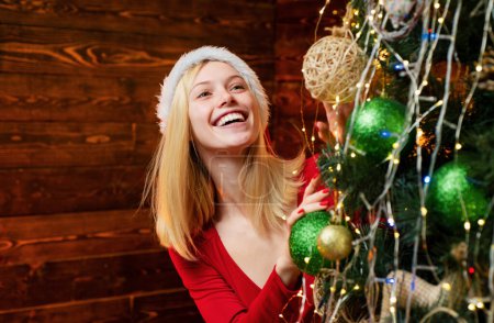Photo for Happy young woman holding Christmas bauble in front of Christmas tree. Beauty girl decorating Christmas tree. Girl is happy about the New Year - Royalty Free Image