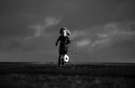 Téléchargez les photos : Un footballeur, un enfant joue au foot. Un gamin de foot jouant au foot. Enfant garçon jouer au football sur le terrain extérieur. Garçon coup de pied ballon de football - en image libre de droit