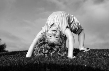 Photo for Happy kid girl standing upside down on her head on grass in summer day - Royalty Free Image
