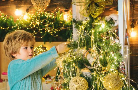 Foto de Niño decorando el árbol de Navidad con chucherías. Decoraciones navideñas. Retrato de Santa niña con adornos mirando a la cámara. Feliz año nuevo - Imagen libre de derechos