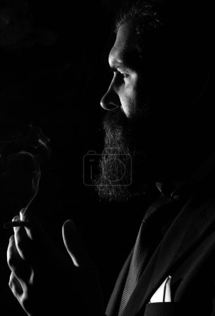 Téléchargez les photos : Un homme d'affaires en costume fumant une cigarette. Fumée sur noir - en image libre de droit