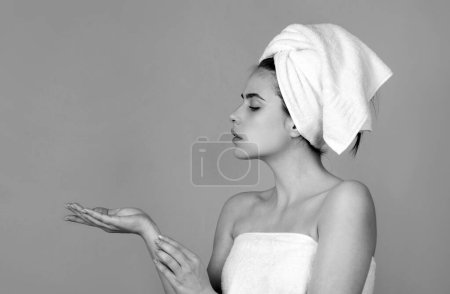 Téléchargez les photos : Portrait of young beautiful woman with cosmetic products. Beauty face of a cheerful attractive girl with towel on head, isolated. Moisturized healthy skin, morning spa, beauty routine, facial - en image libre de droit