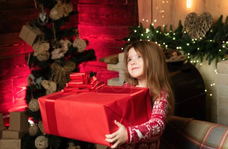 Foto de Alegre niño lindo abriendo un regalo de Navidad. La niña presenta su regalo con una cara agradecida. La verdadera alegría de la Navidad - Imagen libre de derechos