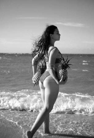 Photo for Sexy woman holding fresh pineapple. Buttocks of girl in bikini with fruit pineapple on beach background, summer vacation, healthy food and fitness - Royalty Free Image