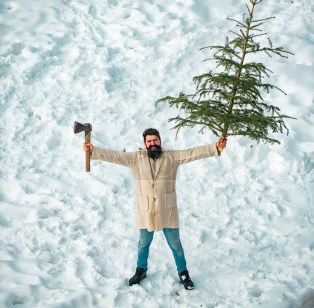 Téléchargez les photos : Joyeux Noël et Joyeuses Fêtes. Émotion hivernale. Portrait d'hiver du bois dans la neige Jardin coupe arbre de Noël. Bûcheron de Noël avec hache et sapin - en image libre de droit