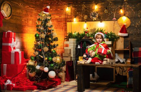 Téléchargez les photos : Cadeaux et surprises. Joyeux Noël et bonne année. Les enfants apprécient les vacances d'hiver à la maison. Fête de la famille Noël. Maison remplie de joie et d'amour. Mignon petit garçon enfant jouer près de l'arbre de Noël. - en image libre de droit