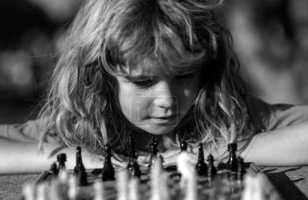Téléchargez les photos : Petit garçon jouant aux échecs en plein air dans le parc. Gros plan sur le visage d'un enfant intelligent intelligent - en image libre de droit