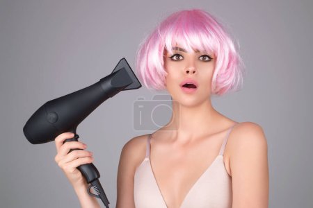 Téléchargez les photos : Belle femme séchant ses cheveux avec un sèche-cheveux isolé sur fond de studio. Jeune femme avec sèche-cheveux sèche-cheveux, faire une coiffure. Gros portrait de fille dans la coiffure de séchage - en image libre de droit