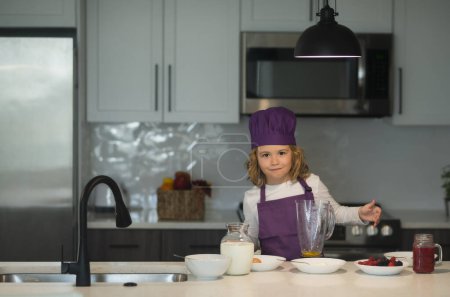 Téléchargez les photos : Chef cuisinier enfant. Petit garçon chef dans tablier et chapeau de chef cuisinier à la cuisine. Aliments sains - en image libre de droit