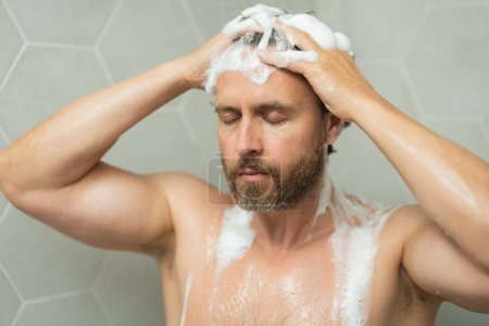 Foto de Hombre hispano lavando el pelo en el baño. Cabezal de ducha en la bañera. Cara masculina en la ducha. Hombre duchándose en el baño. Un tipo duchándose. Concepto de baño. El hombre está bajo gotas de agua en el baño - Imagen libre de derechos