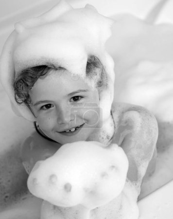 Téléchargez les photos : Les enfants sont en mousse. Enfant se baignant dans un bain avec de la mousse. Drôle de visage d'enfant baigné dans le bain - en image libre de droit