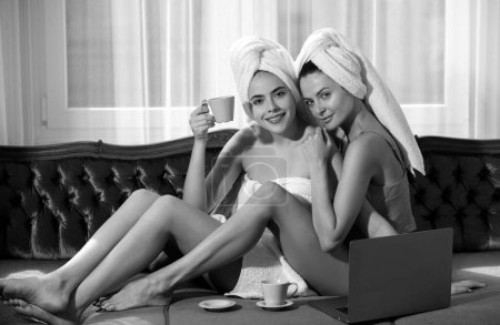 Foto de Señoras alegres bebiendo café, dormitorio interior. Chicas amigas disfrutando del día de la mañana en casa juntas, tumbadas en la cama y relajadas. Buenos días chicas hablando - Imagen libre de derechos