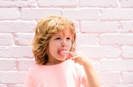 Téléchargez les photos : Crème glacée enfant. Petit garçon mangeant de la crème glacée dans un fond rose - en image libre de droit