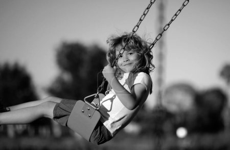 Téléchargez les photos : Petit garçon s'amusant sur une balançoire sur l'aire de jeux dans le parc public le jour de l'été. Un enfant heureux aime se balancer. Enfant jouant à l'aire de jeux dans le jardin. Les enfants s'amusent sur l'aire de jeux - en image libre de droit