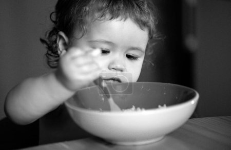 Photo for Kid baby eat soup in the kitchen with dishes and spoon - Royalty Free Image