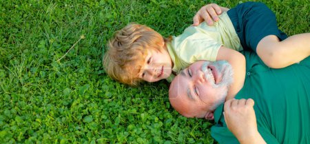 Foto de Feliz abuelo y nieto relajándose juntos en la hierba. Niño con el abuelo sueña en verano en la naturaleza. Abuelo y nieto, bandera de primavera - Imagen libre de derechos
